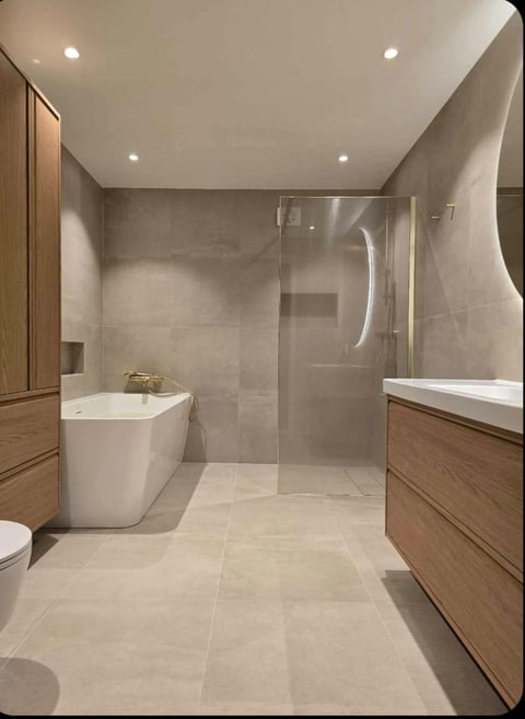 Modern bathroom with beige tiles, wooden vanity, white freestanding bathtub, and glass shower enclosure