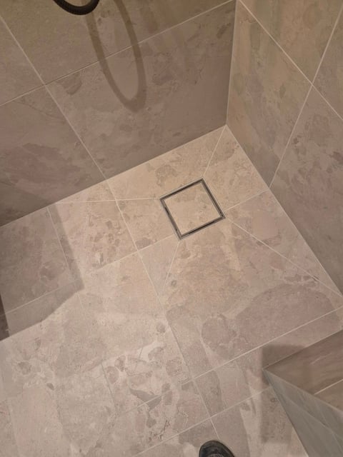 Modern tile shower floor with centered square drain and walls tiled in beige marble-look ceramic tiles