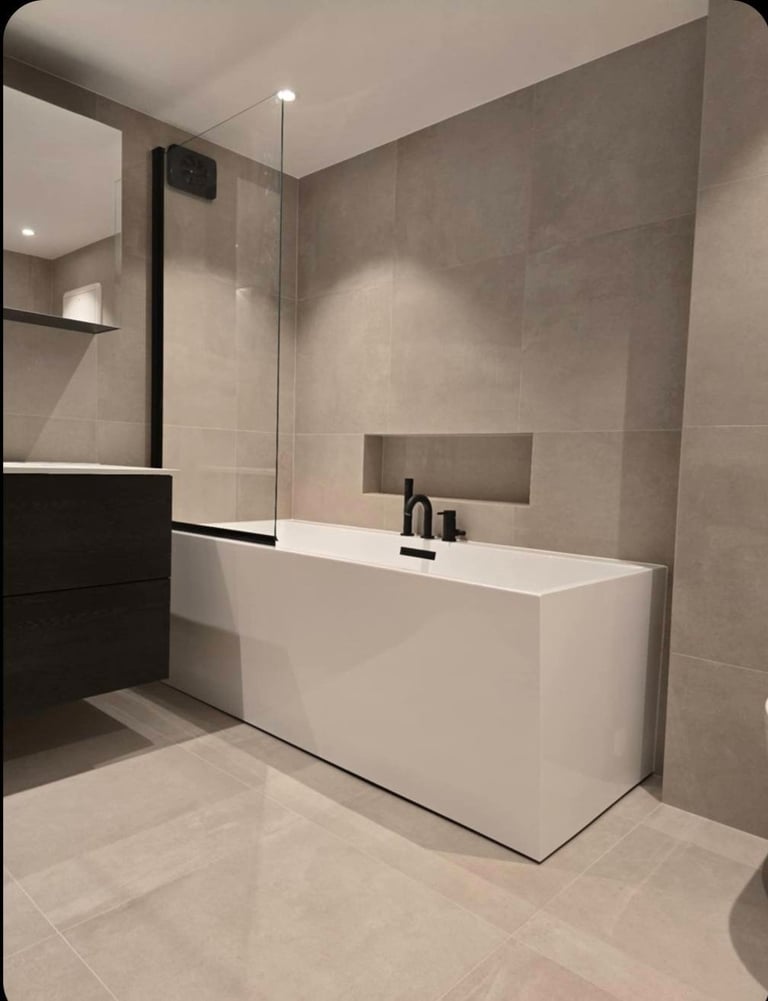 Modern bathroom with white freestanding tub, glass shower partition, beige tile walls, and black vanity sink
