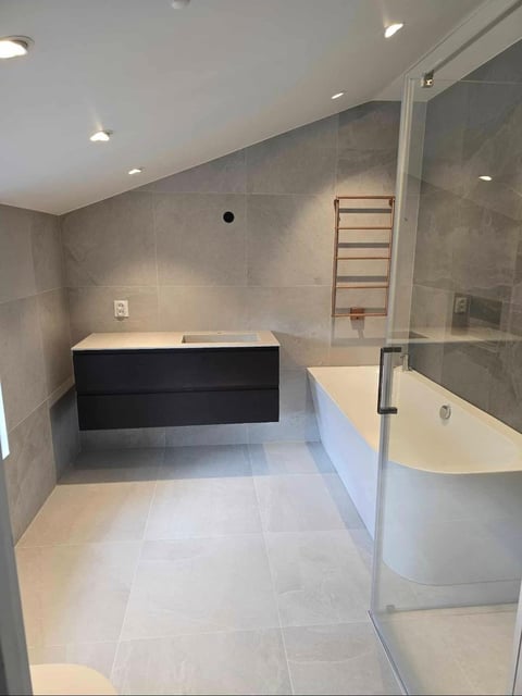 Modern bathroom with gray tile walls, black soaking tub, glass shower enclosure, and light stone flooring