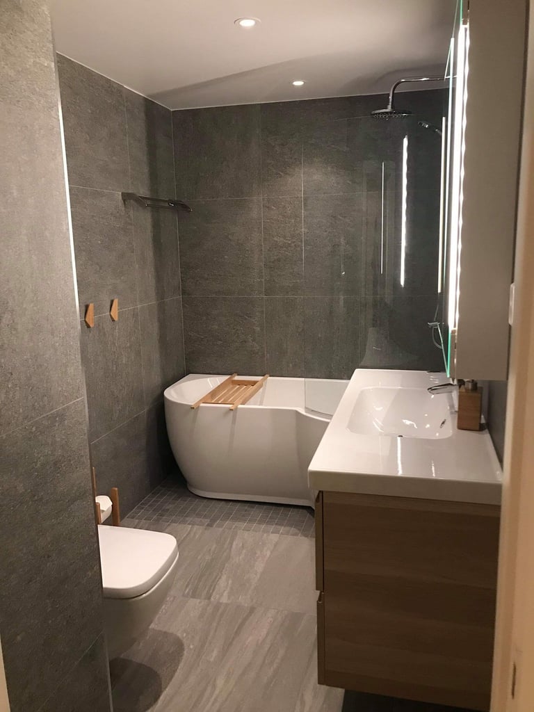 Modern bathroom with freestanding white soaking tub, floating vanity sink, dark tile walls, toilet, and recessed lighting