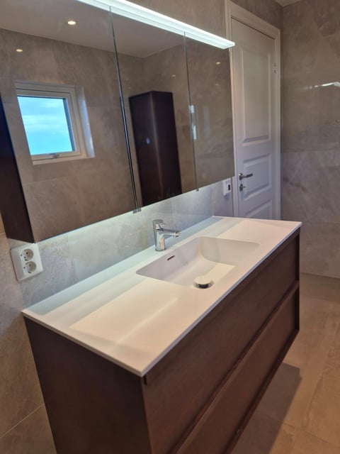 Modern bathroom vanity with white sink, dark wood cabinet, and large mirror with overhead lighting