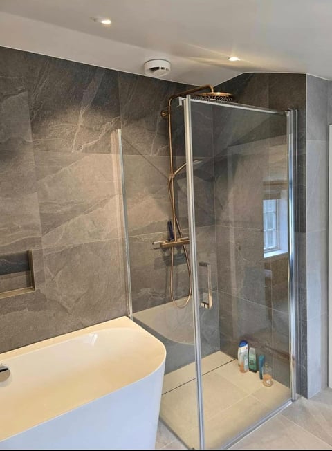 Modern bathroom with walk-in shower enclosed by glass doors and walls with slate tile, next to white freestanding soaking tub
