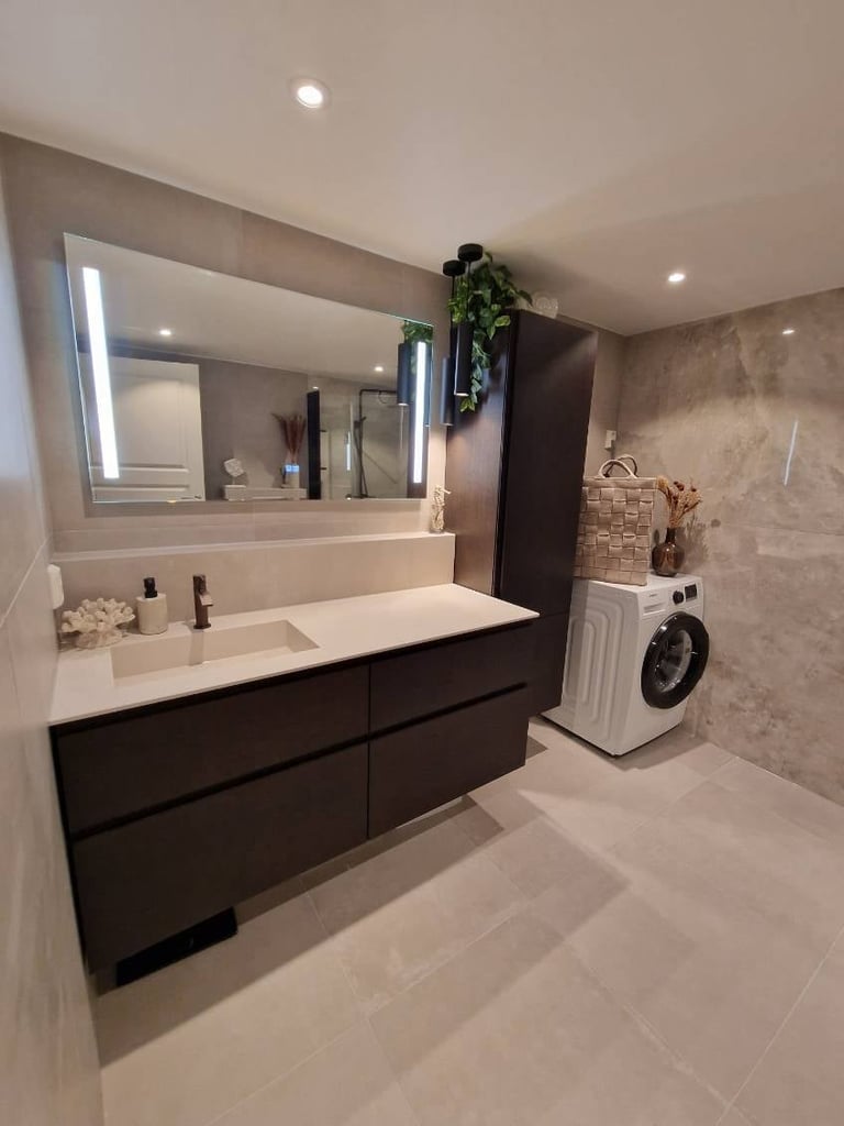 Modern bathroom with double sink vanity, black cabinetry, large mirror with lighting, washing machine, and neutral tiled flooring