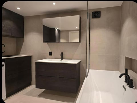 Modern bathroom with dark wood vanity, large mirror, white sink, walk-in shower with glass enclosure, and neutral tile walls