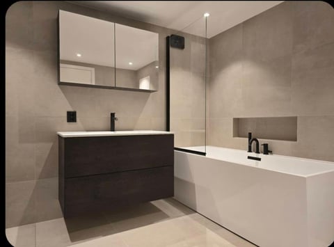 Modern bathroom with dark vanity, mirror cabinet, white bathtub, and glass shower enclosure in neutral beige tones