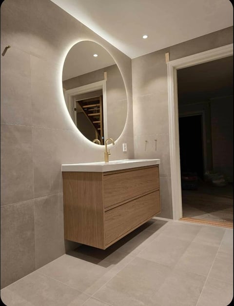 Modern bathroom with wooden vanity, white countertop, and oval illuminated mirror mounted above sink