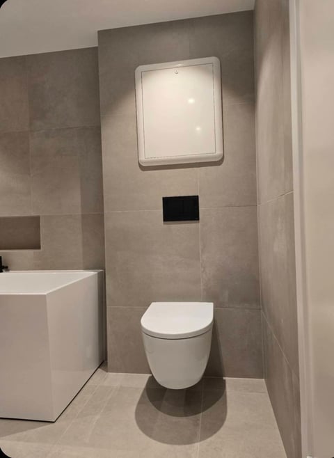 Modern bathroom with white wall-mounted toilet, illuminated mirror, and beige tile walls