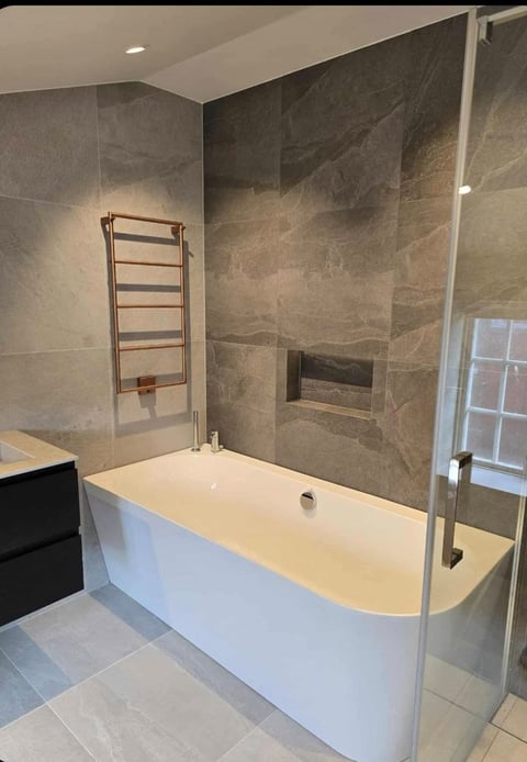 Modern bathroom with white soaking tub, gray tile walls, glass shower enclosure, heated towel rack, and recessed lighting