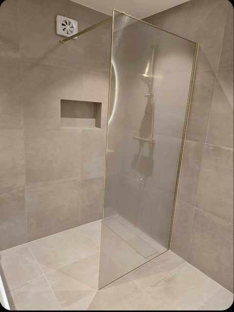 Modern bathroom walk-in shower with glass enclosure, beige tile walls, built-in niche, and ventilation fan